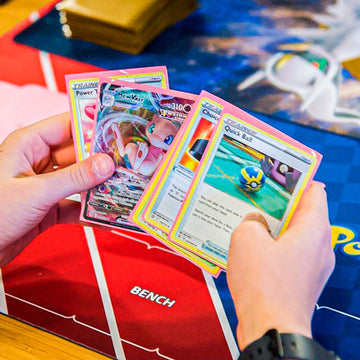Hands holding colorful trading cards over a red 'Bench' area, with a blue mat in the background.